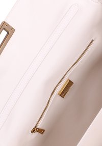 Interno di una borsa a mano in pelle bianca con una zip dorata dotata di un pull tab, un accento in hardware dorato e una finitura leggermente testurizzata.
