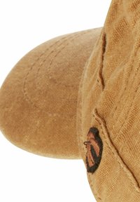 Tan fabric cap with a curved brim, featuring textured surface detailing and a small black and orange embroidered accent on the side.