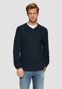 Marineblauer Strickpullover mit Diamantmuster, V-Ausschnitt, gerippten Bündchen und Saum, kombiniert mit hellblauen Jeans. Strukturiert gewebter Stoff.