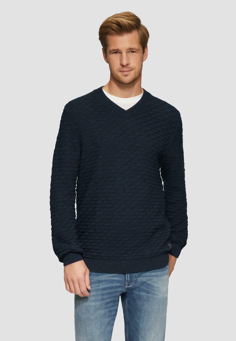 Marineblauer Strickpullover mit Diamantmuster, V-Ausschnitt, gerippten Bündchen und Saum, kombiniert mit hellblauen Jeans. Strukturiert gewebter Stoff.