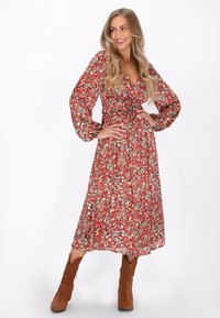 Rochie roșie, cu model, cu mâneci lungi și umflate și talie cu șnur. Lungime midi, cu un design floral în tonuri de verde și albastru. Botine din suedi brown.