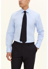 Ljusblå skjorta med långa ärmar och ett svart slips. Skjortan har en spetsig krage och en jämn tygtextur, kombinerad med mörka byxor.