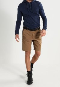 Granatowa koszula z długim rękawem i kapturem, khaki szorty z paskiem, czarne trampki. Codzienny strój o luźnym kroju, podkreślający wygodę i funkcjonalność.