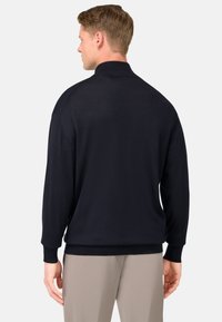 Mörkblå långärmad tröja med hög krage, ribbade ärmslut och nederkant. Mjuk textur med avslappnad passform. Bakifrån visas minimal detaljering.