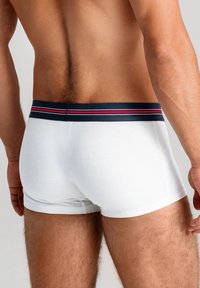 Vita bomullboxershorts med en marinblå midjeband som har röda och vita ränder, med en närbild av baksidan och benens detaljer.
