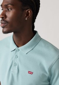 Light blue polo shirt with a textured design, three buttons, and a red Levi's logo patch on the left chest. Short collar and sleeves.