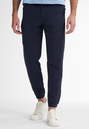 Marine joggers van zacht materiaal met een taps toelopende pasvorm. Voorzien van ritszakken aan de zijkant en geribbelde boorden. Gecombineerd met witte sneakers.