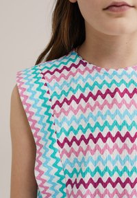 Top sin mangas multicolor con un patrón de zigzag en rosa, púrpura, turquesa y blanco. Tejido texturizado con un escote redondeado.