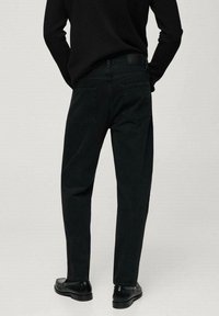 Vaqueros de mezclilla negros con corte recto, que cuentan con dos bolsillos traseros y detalles de costura sutiles. Llevado con una blusa negra y zapatos.