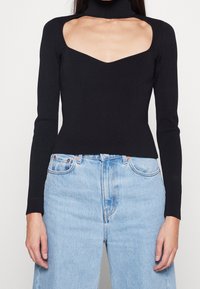 Svart ribbad långärmad topp med hög krage och fyrkantig halsringning, kombinerad med ljusblå högmidjade jeans.