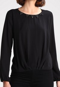 Maglietta nera a maniche lunghe con scollatura rotonda e dettagli decorativi in perline, design con vita arricciata. Tessuto liscio e leggero.
