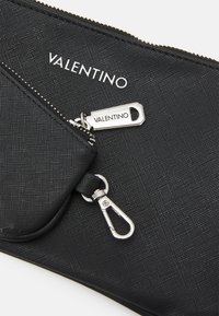 Pochette nera testurizzata con zip argentata, dotata di una piccola tasca esterna e un gancio per le chiavi. Logo "VALENTINO" ben in evidenza.