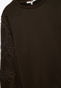 Sudadera marrón oscuro con un diseño floral texturizado en la manga izquierda. Presenta un cuello redondo y una tela suave y lisa.
