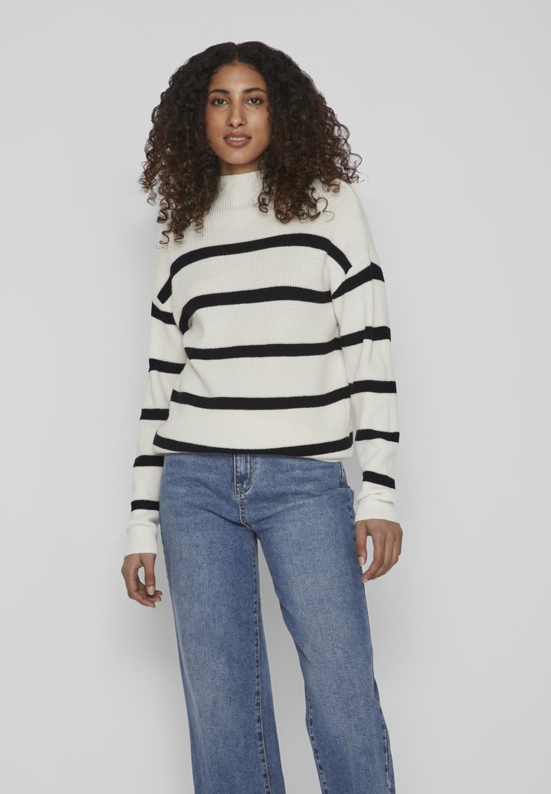 Cream striped sweater with black horizontal stripes, ribbed texture, high neckline, paired with light blue wide-leg jeans.