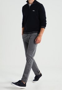 Marinblå zip-up tröja med vita detaljer, matchad med ljusgrå slim-fit byxor och mörka sneakers, vilket skapar en avslappnad look.