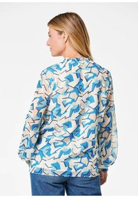 Durchsichtige Bluse mit einem mehrfarbigen geometrischen Muster in Blau, Creme und einem Hauch von Braun. Rüsche am Ausschnitt und lange Ärmel.