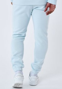 Lichtblauwe joggingsbroek van zachte stof, met elastische boorden. Gekleed met witte sneakers. Eenvoudige, gladde textuur met een aansluitend ontwerp.