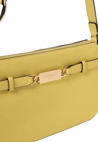 Borsa a tracolla in pelle gialla con una placca logo in tono oro e una tracolla regolabile, caratterizzata da una texture liscia e un design elegante.