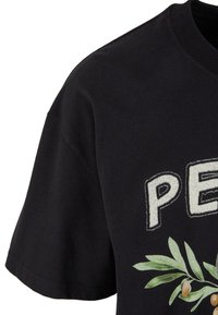Zwarte katoenen t-shirt met korte mouwen, voorzien van witte lettering en een groen blad grafisch detail met olijven. Ronde hals, ontspannen pasvorm.