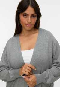 Lichtgrijze cardigan met een diepe V-hals, lange mouwen en een zachte structuur. Draagt over een wit topje met minimalistische ontwerpdetaillering.