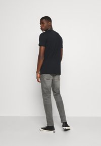 Black short-sleeve t-shirt, slightly longer in back, paired with gray slim-fit jeans and black high-top sneakers. Smooth fabric, casual design.