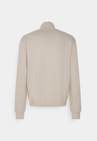 Felpa beige con colletto alto, maniche lunghe e polsini a costine. Realizzata in un tessuto morbido con una superficie liscia.