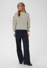 Langärmeliges gestreiftes Shirt in Creme und Marineblau, kombiniert mit marineblauen Hosen. Das Shirt verfügt über ein kleines Logo auf der Brust und einen lockeren Sitz.