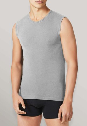 Uomo con indosso una maglietta grigia senza maniche e pantaloncini aderenti neri, in piedi con le braccia rilassate contro uno sfondo chiaro e uniforme.