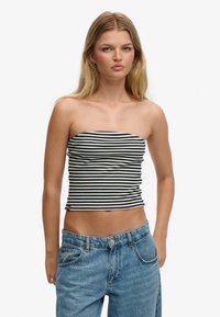 Top corto a rayas, sin tirantes, en negro y blanco; tela elástica con silueta ajustada, combinado con vaqueros azul de cintura alta.