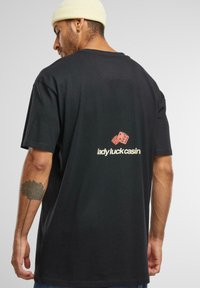 Tricou scurt, negru, cu mânecă scurtă, având o grafică cu zaruri roșii și textul "lady luck casin" imprimat în alb pe partea din spate. Material din bumbac.