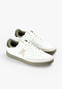 Un par de zapatillas deportivas blancas de corte bajo con suelas beige, logotipo de calavera y huesos cruzados en el lateral, y forro interior en verde olivo.