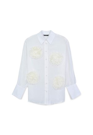 White button-up shirt with long sleeves, featuring textured white floral appliqués on the chest. Smooth fabric and classic collar design.