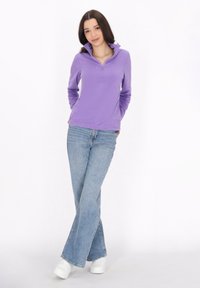 Pullover viola con colletto zip, maniche lunghe. Abbinato a jeans a zampa d'elefante blu chiaro e sneakers bianche. Tessuto liscio, vestibilità casual.