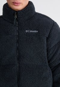 Zwarte fleecejack met hoge kraag, ritssluiting aan de voorkant en het Columbia-logo. Getextureerde stof met een zachte, pluizige uitstraling.