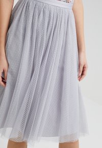 Falda de tul gris claro con un patrón de lunares texturizados, que presenta una cinturilla suave y un diseño fluido que añade volumen.