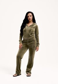 Olívazöld velúr melegítő, rövidített cipzáras kapucnival és hozzáillő nadrággal. Jellegzetességei a húzózsinórok és az oldalzsebek.