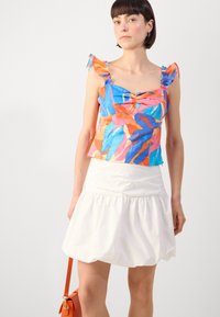 Top sans manches coloré avec des bretelles à volants, présentant un motif de feuilles bleu, rose et orange. Associé à une jupe évasée blanche.