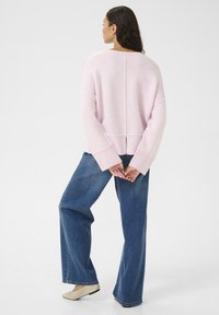 Maglione oversized rosa chiaro con un ampio orlo a coste e polsini, abbinato a jeans blu larghi e scarpe basse crema, visto da dietro.