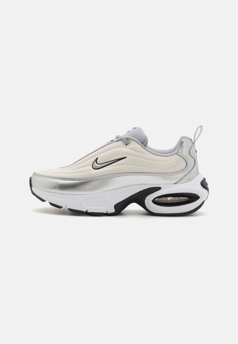 Zapatilla Nike con una parte superior suave y blanca, acentos plateados y una suela de goma negra. Presenta amortiguación Air y un diseño aerodinámico.