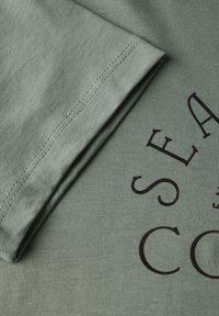 Zelené bavlněné tričko s hladkým povrchem, s ohnutým rukávem a černým potiskem na přední straně.