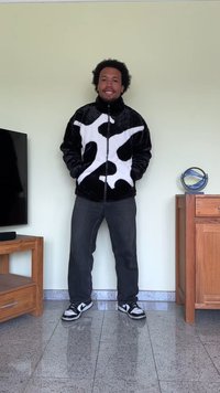 Svart-hvitt ku-mønstret glidelåsjakke laget av myk stoff, sammen med mørke bukser og svarte joggesko med hvite detaljer.