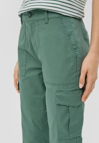 Grüne Cargo-Hosen aus Baumwolle, mit geradem Bein, seitlichen Taschen und Knopfverschluss, sowie sichtbaren Steppnähten.