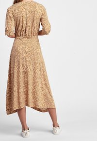 Vestido midi marrón con flores, de mangas cortas, cintura ceñida y dobladillo curvado, hecho de tejido ligero; combinado con zapatillas blancas.