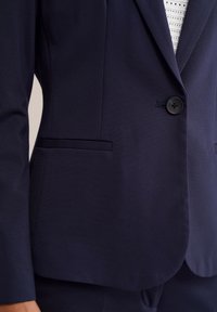 Mörkblå blazer med en enda svart knapp, sidofickor och en slät yta, visad framifrån i axel- och brösthöjd.