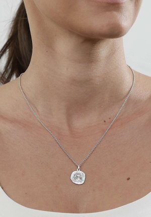 Silberne Kettenhalskette mit rundem, strukturiertem Anhänger, der ein erhabenes Pferdemotiv zeigt, getragen an Hals und oberer Brust einer Frau.