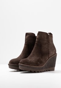 Bruna mockaskinnskängor med kilklack och en texturerad plattform, rund tå, dekorativ sömnad och en dragflik på baksidan för enkel påtagning.