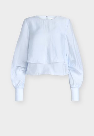 Blouse courte bleu clair avec un col rond, des manches longues froncées, et un design superposé. Confectionnée dans un tissu lisse avec un léger éclat.