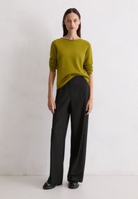 Pull en tricot vert olive avec des manches retroussées, associé à un pantalon large noir et des chaussures noires. Design simple, moderne et ajusté.
