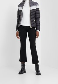 Padded jacket in gray and white, zip-front with gold accents, styled over a white turtleneck. Paired with black flared trousers and black boots.