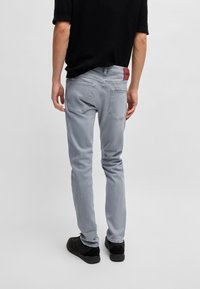 Ljusgrå jeans med smal passform, detaljerad sömnad, två bakfickor och en röd logotypmärke vid midjan. Bärs med en svart topp och skor.